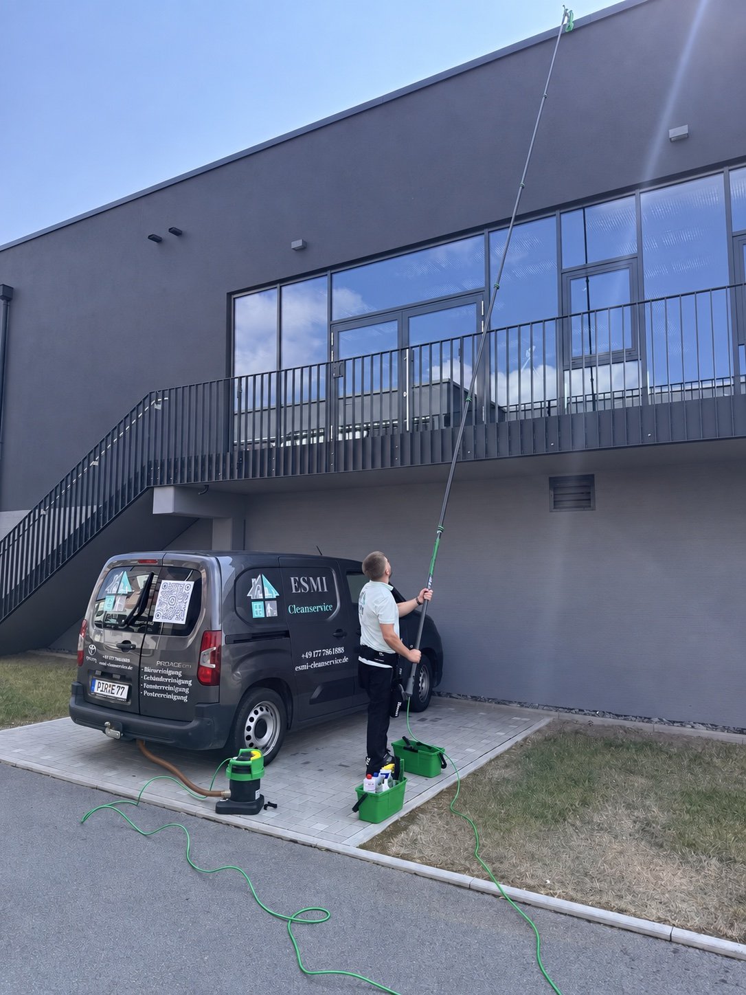 ESMI Cleanservice bei der Fensterreinigung mit Teleskopstange und Wasserfilter neben dem Firmenfahrzeug