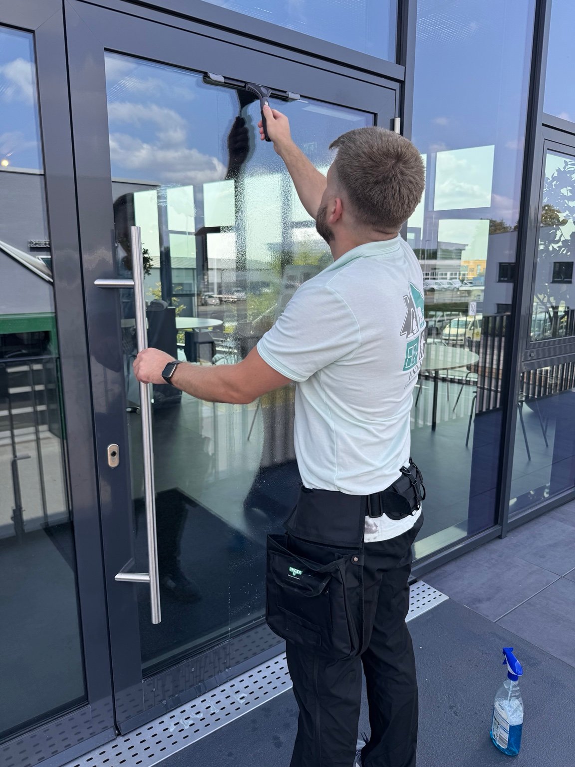 Mitarbeiter von ESMI Cleanservice reinigt eine Glastür mit einem Fensterabzieher